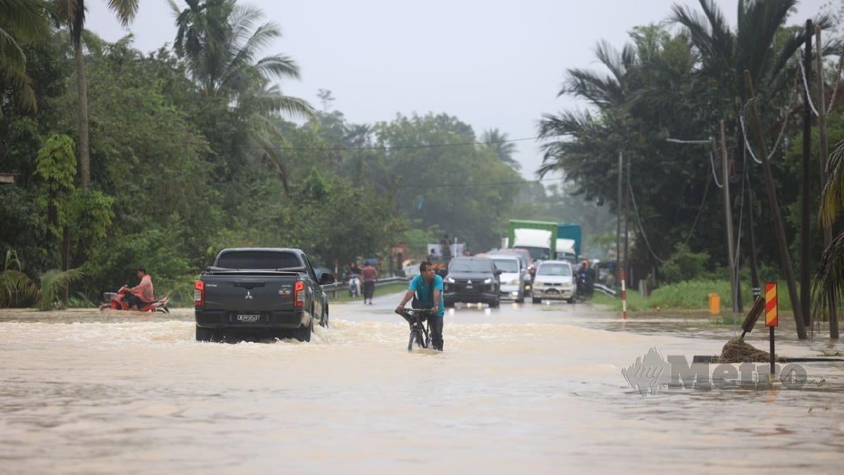 Penduduk meredah banjir kilat yang melimpahi jalan utama di Kampung Bukit Abal, hari ini. FOTO NIK ABDULLAH NIK OMAR