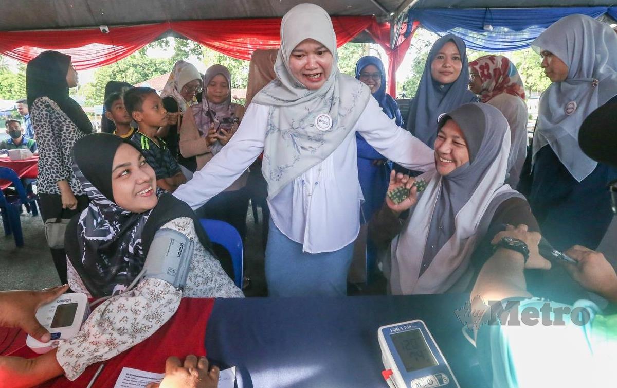 FADHLINA Sidek (berdiri tengah) beramah mesra dengan penduduk yang melakukan pemeriksaan kesihatan di Kampung Sungai Duri di sini. FOTO Danial Saad