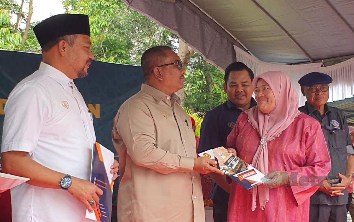 NORASHIKIN, menerima geran hak milik tanah daripada Datuk Seri Muhammad Sanusi (dua dari kiri) pada Majlis Penyerahan Geran di Surau Al-Muhtadin. FOTO Hamzah Osman