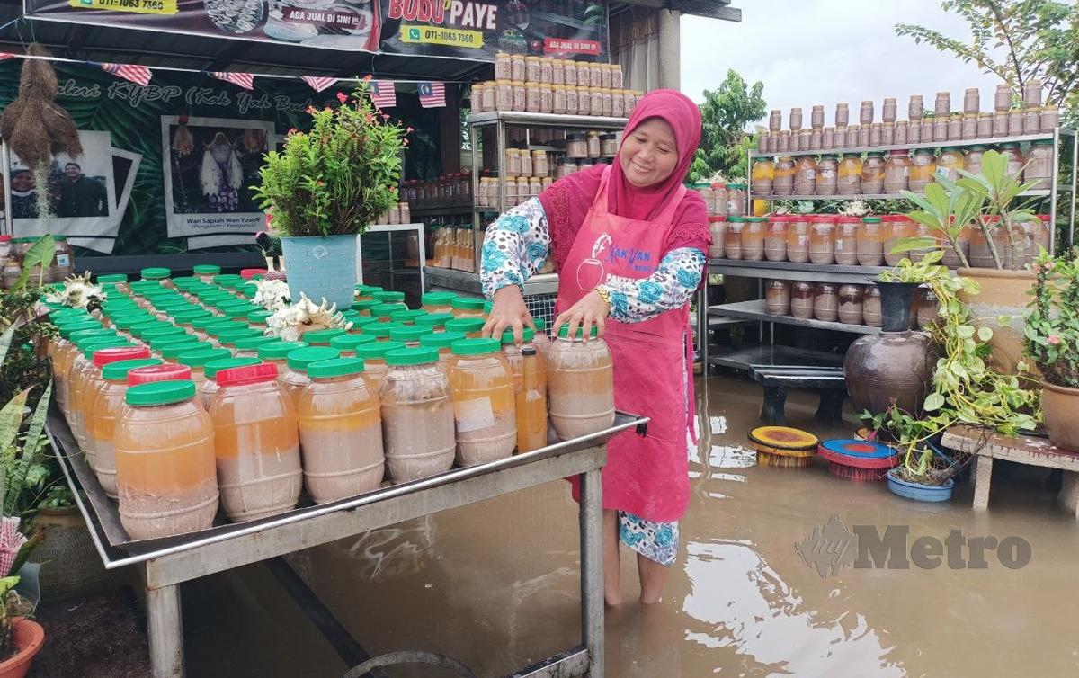 SAPIAH mengemas dan memindahkan 500 botol budu tempayan kerana bimbang dihanyutkan air banjir di premisnya di Pantai Geting. FOTO Siti Rohana Idris