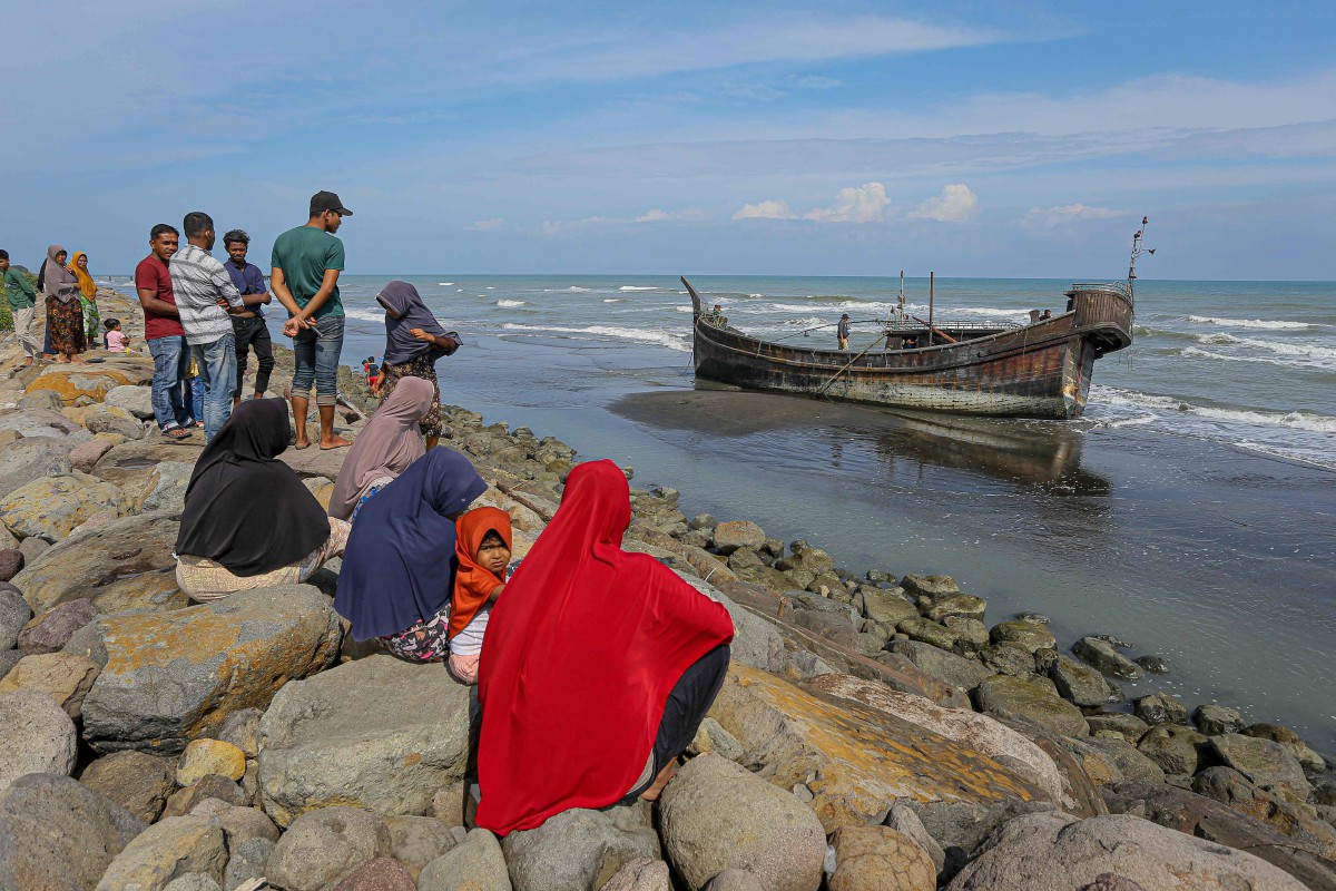 Penduduk tempatan melihat kapal yang digunakan pendatang Rohingya di Pidie, Aceh. - FOTO AFP