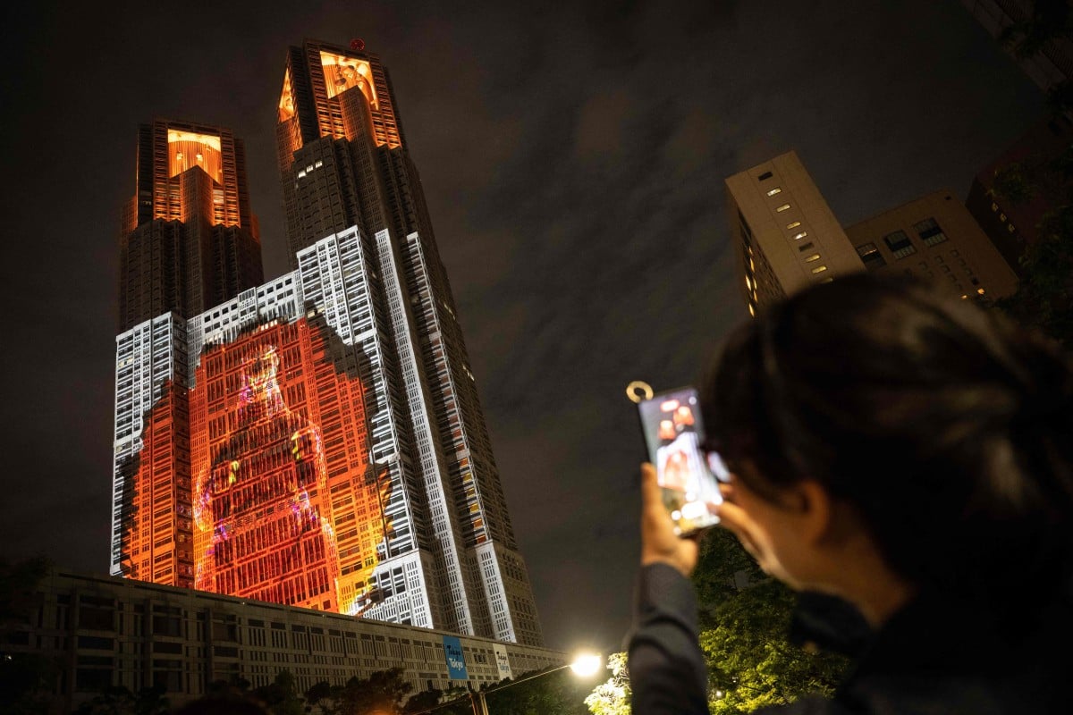 Orang ramai mengambil gambar imej digital Godzilla setinggi 100 meter di Tokyo, Jepun. - FOTO AFP