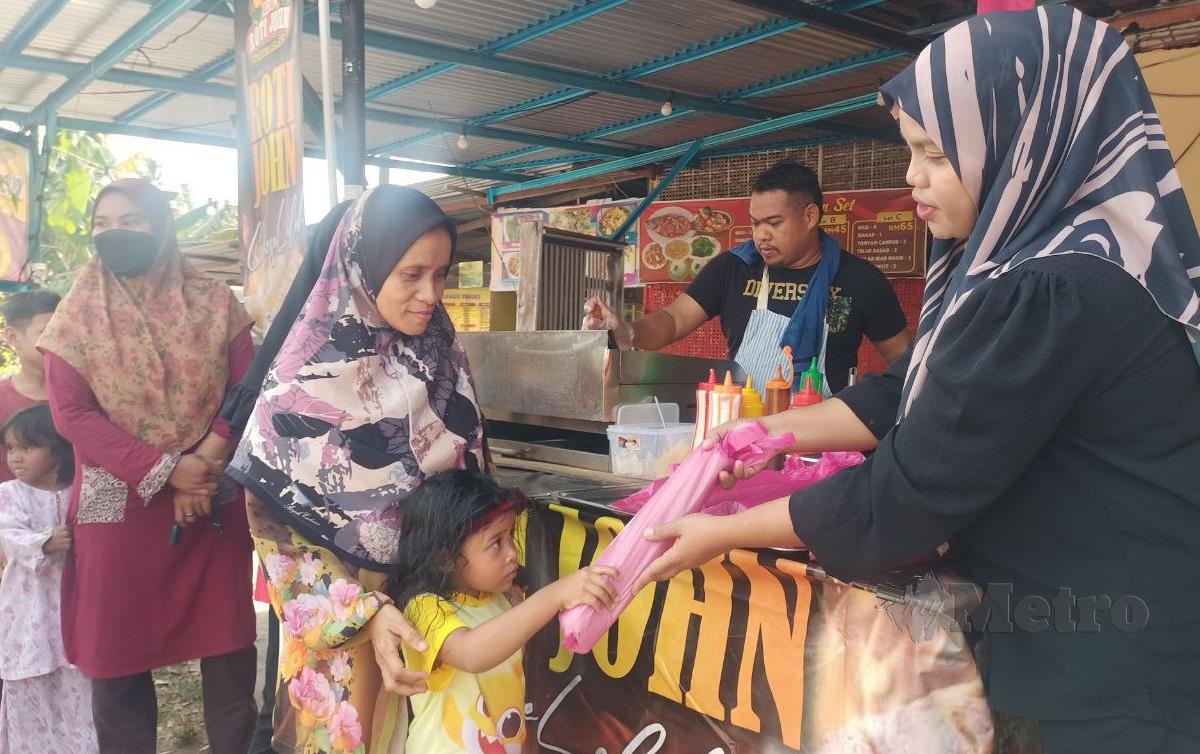 MAHIRRAN (baju hitam) mengagihkan roti john percuma kepada asnaf di gerainya. FOTO Siti Rohana Idris