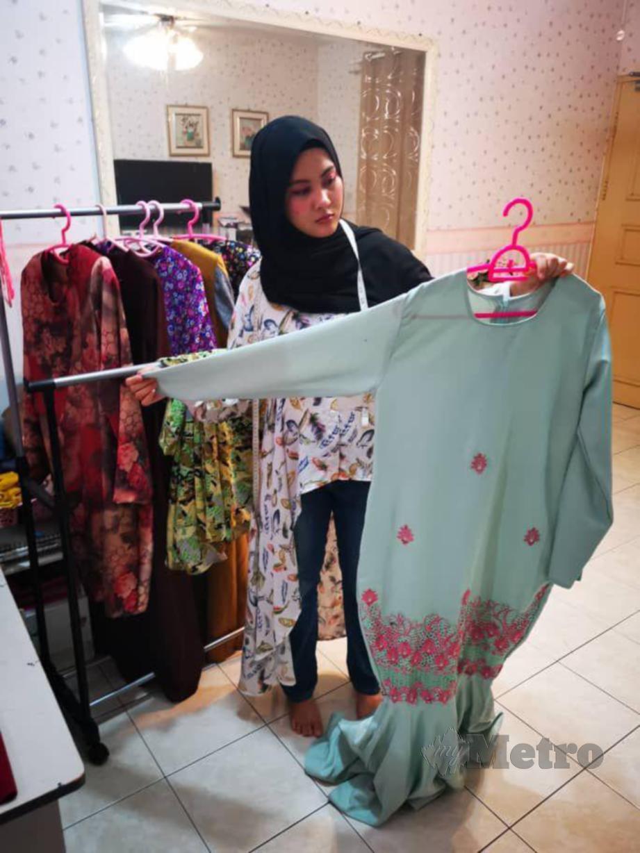 FATIN Syahirah meneliti baju raya pelanggannya yang sudah siap dijahit. FOTO Yun Mikail