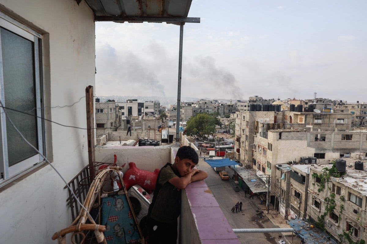 Seorang budak lelaki berdiri di atas balkoni dengan pemandangan asap berkepul-kepul akibat serangan Israel di bandar Rafah di selatan Semenanjung Gaza pada 28 Mei 2024. FOTO Eyad BABA/AFP)