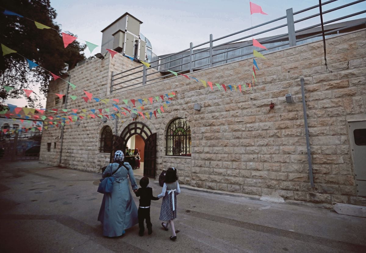 Seorang ibu Palestin dan anak-anaknya berjalan kaki di luar teater kebangsaan Palestin. FOTO AFP