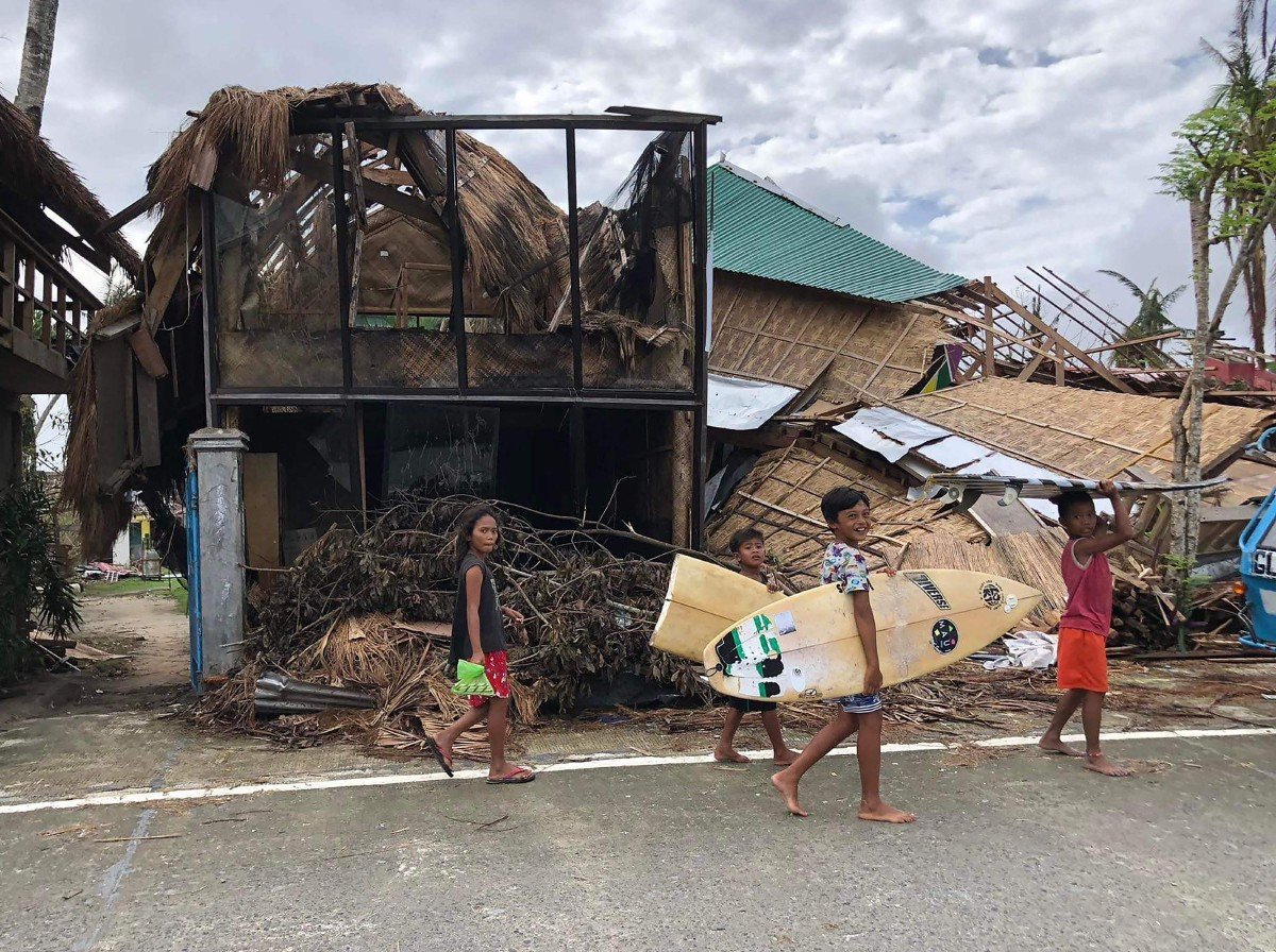 Kanak-kanak membawa barangan peribadi mereka berjalan di hadapan rumah yang musnah dipukul Taufan Rai di bandar General Luna, pulau Siargao. - FOTO AFP