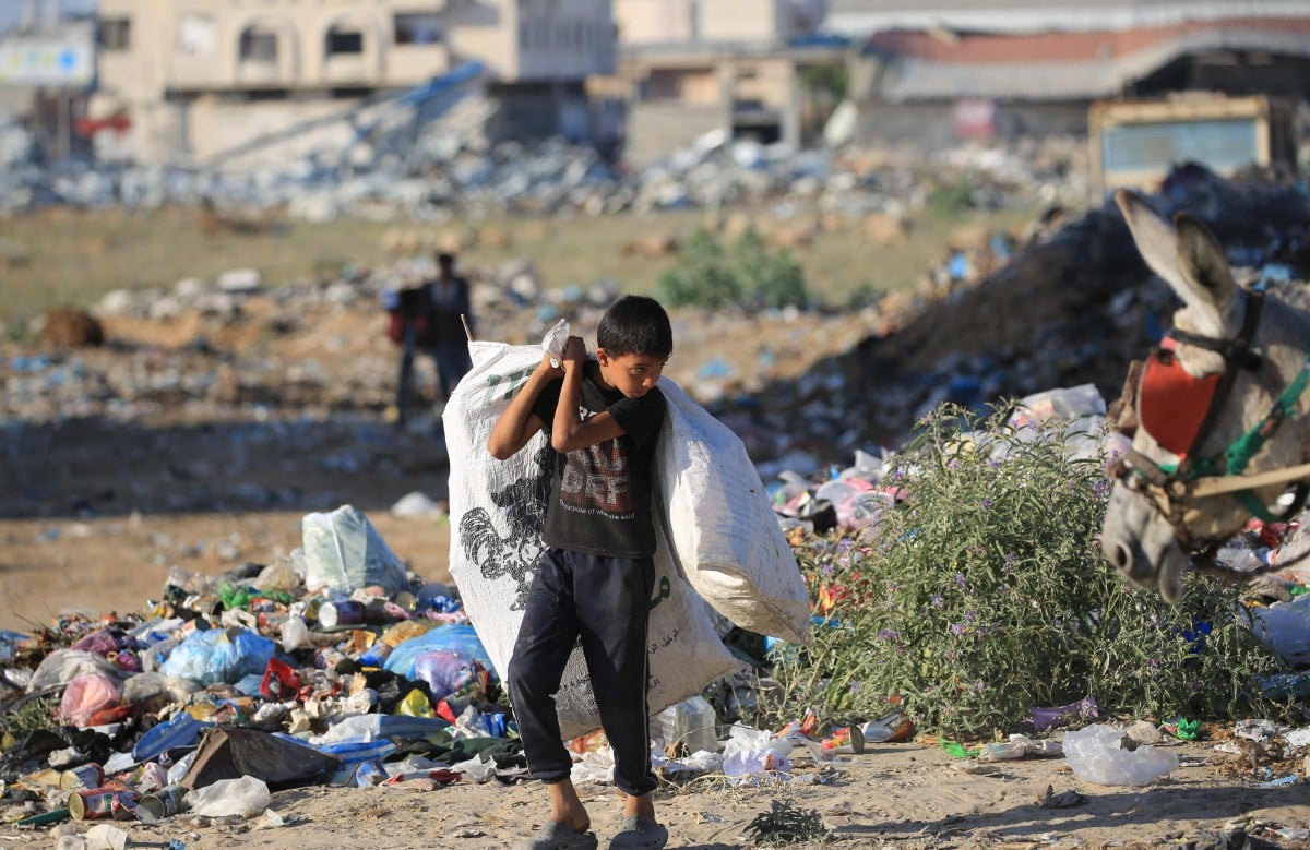 Penduduk Palestin membawa beg berjalan melepasi tempat pembuangan sampah di kem pelarian al-Maghazi di tengah Semenanjung Gaza pada 5 Jun 2024. FOTO Eyad BABA /AFP