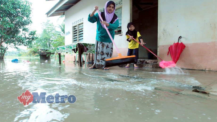 Nur Azlina bersama seorang anaknya membersihkan rumah mereka di Kampung Kajang Sebidang, Tumpat selepas banjir semakin surut. FOTO Syamsi Suhaimi