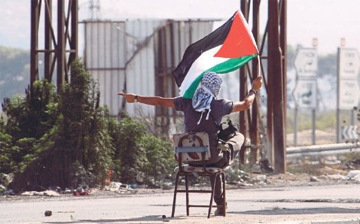 SEORANG remaja mengibarkan bendera Palestin sambil memerhatikan pertempuran antara rakannya dengan tentera Israel di Howara, berhampiran Nablus, bandar di Tebing Barat.