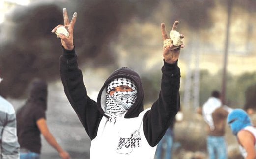 REMAJA Palestin menunjukkan tanda kejayaan sementara sebelah tangannya memegang batu yang akan digunakan untuk menyerang tentera Israel di Beit El, Ramallah.