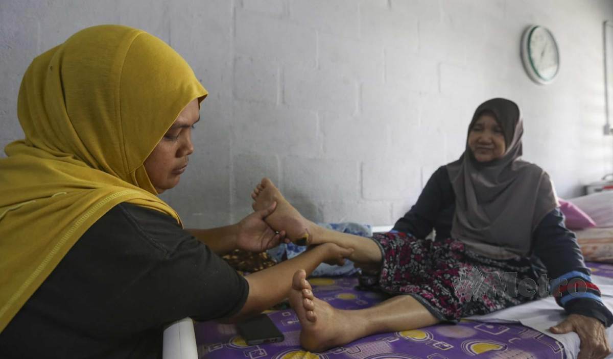 ROSFAZILAH (kiri) yang mempunyai kekurangan dari segi fizikal akibat kesan diserang strok menunjukkan kesan melecur pada kaki ibunya, Rubiah mengalami kencing manis, ketika ditemui di kediaman mereka. FOTO Azrul Edham Mohd Aminuddin 
