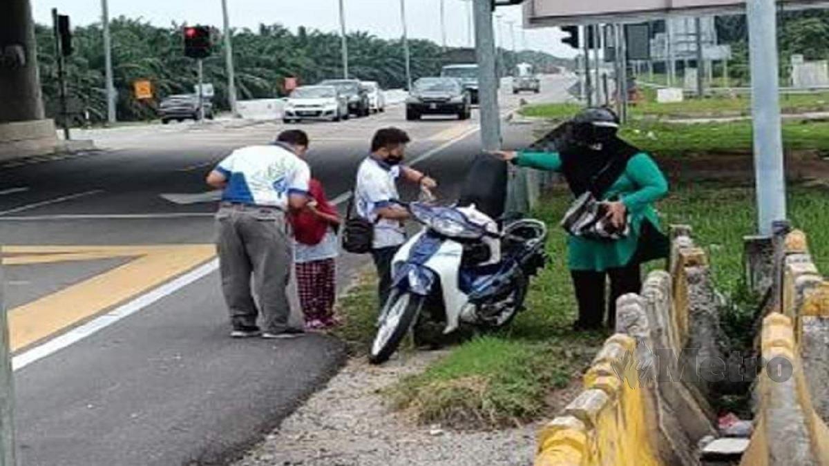Dua kakitangan LZS membantu dua beranak yang motosikal mereka kehabisan petrol di jalan menghala ke Ijok, semalam. FOTO ihsan LZS