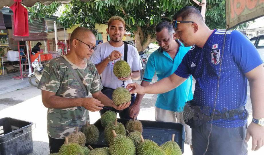 KHAIRIL Anuar (kiri ) membantu pelanggan memilih durian digerainya di Kampung Chennah. FOTO Abnor Hamizam