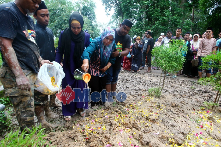 Mariah Senawi, 45, (tengah) menyiram air di pusara Siti Asmah. FOTO Azhar Ramli