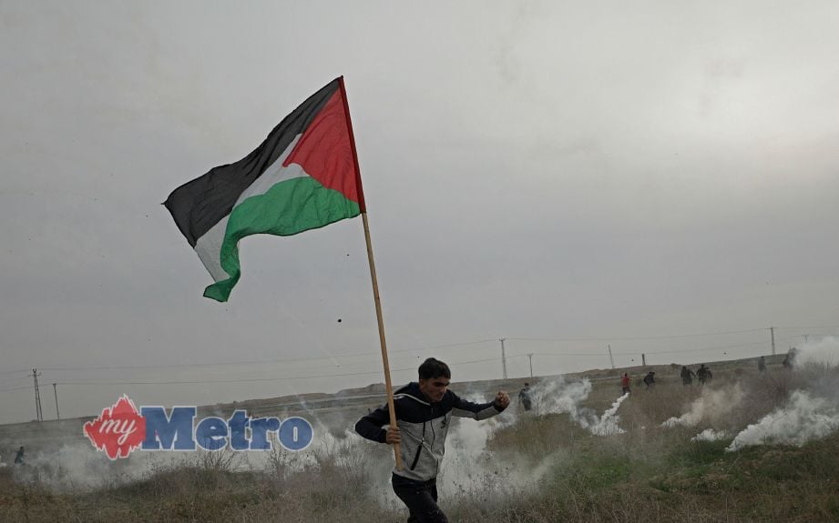 Seorang rakyat Palestin membawa bendera negaranya ketika menyelamatkan diri daripada serangan gas pemedih mata oleh tentera Israel di Gaza pada 22 Disember 2017. FOTO Agensi
