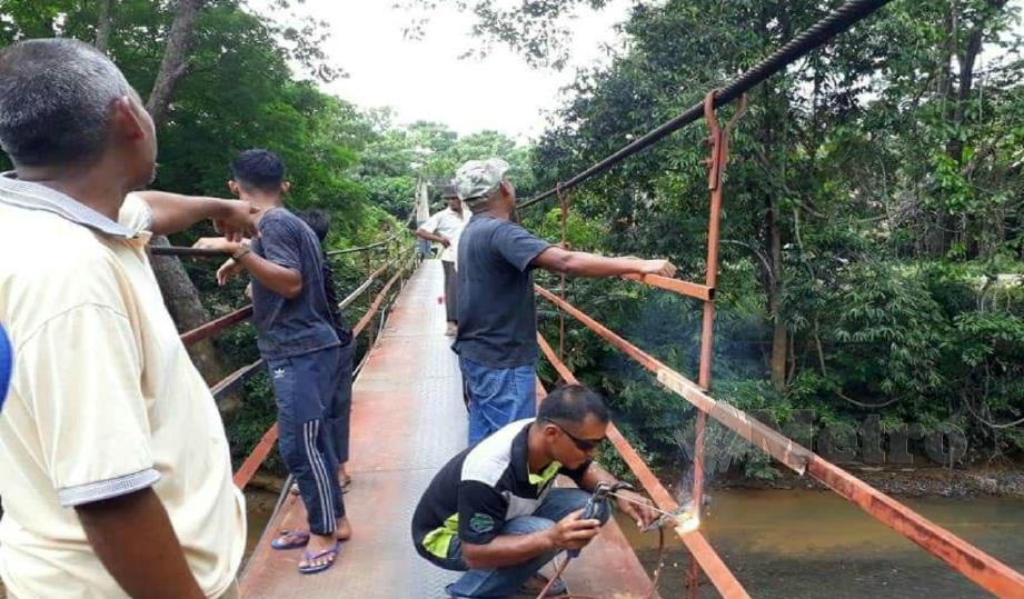 PENDUDUK membaiki jambatan gantung di Kampung Batu Papan. FOTO Ramli Ibrahim.