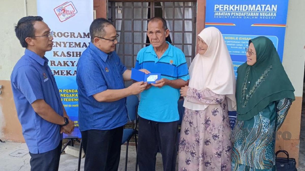 ZAMRI menyerahkan kad pengenalan kepada Abdul Wahab pada Program Menyemai Kasih Rakyat (MEKAR) di Kampung Telaga Daing, hari ini. FOTO Faizaul Azlan Razak