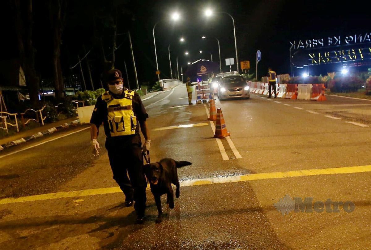 Pengendali K9, Koperal Navindran Rajagopal menggunakan anjing pengesan yang dikenali sebagai 'Yaiko' bagi membendung kemasukan dadah di pintu masuk utara Perak pada sekatan jalan raya (SJR) berikutan sekatan pergerakkan di daerah Kerian. FOTO SHARUL HAFIZ ZAM