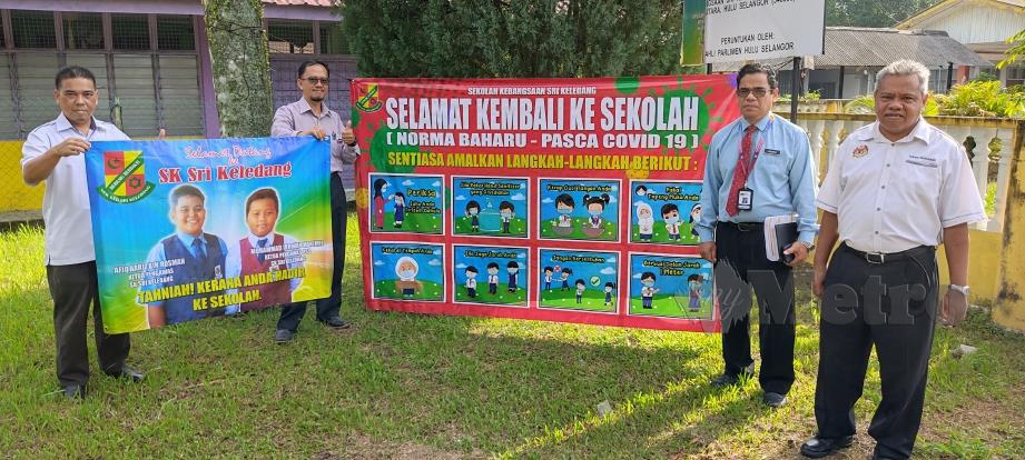 Ahmad Shauhada (kanan) dan Zulkifli (dua dari kanan) dari PPD Hulu Selangor bersama kain rentang yang dipasang di pintu masuk sekolah. FOTO Rosman Shamsudin 