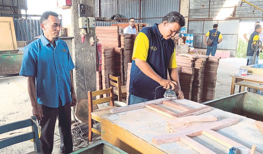 PENGARAH Urusan Bidin Bin Jasin Sdn Bhd, Zaharin Bidin (kiri) melihat pekerja membuat kerusi berasaskan kayu.