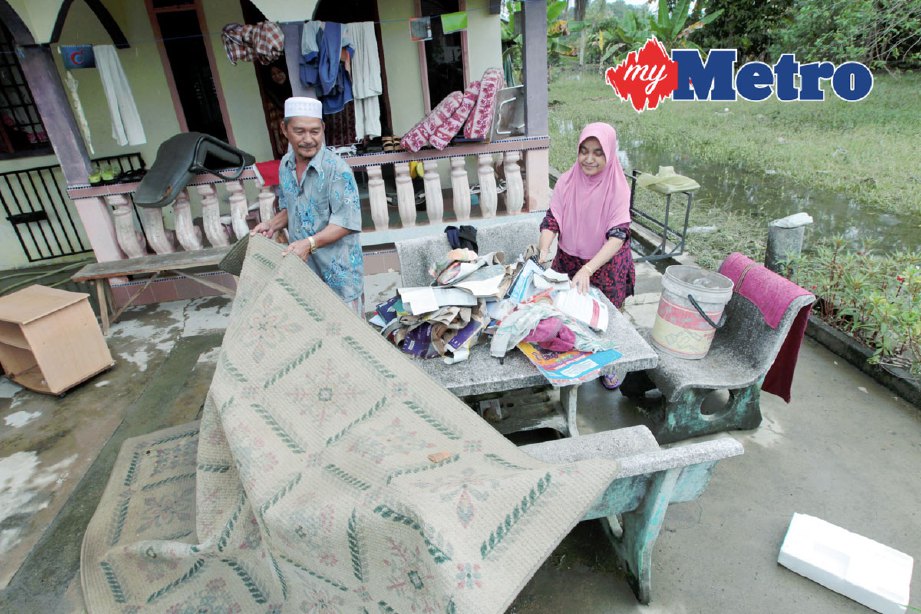 Mangsa banjir, Noriah Che Wan, 57, bersama suaminya, Mohd Yaacob, 61, menjemur barangan yang ditenggelami air selepas air banjir mulai surut di rumahnya di Kampung Belimbing, Kota Bharu. FOTO SYAMSI SUHAIMI