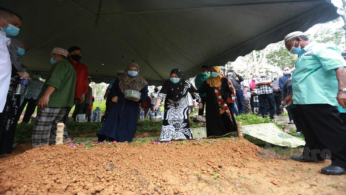 Isteri kedua Allahyarham Datuk Hasbullah Osman, Zaini Abu Bakar (tengah) menyiram air mawar di pusara. FOTO SHARUL HAFIZ ZAM