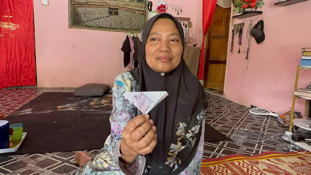 Azizah menunjukkan duit RM100 yang diberikan arwah suaminya ketika ditemui di rumahnya di RKT Jeram Tekoh, di sini. Foto Paya Linda Yahya 