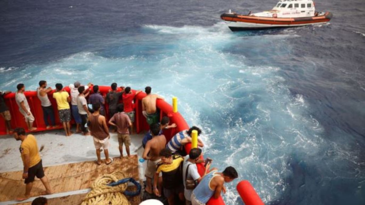 Migran di atas kapal penyelamat NGO Proactiva Open Arms Uno melihat bot Guardia Costiera menuju ke pulau Lampedusa, di tengah Laut Mediterranean, berhampiran pulau Lampedusa, Itali, 19 Ogos 2022. FOTO AGENSI