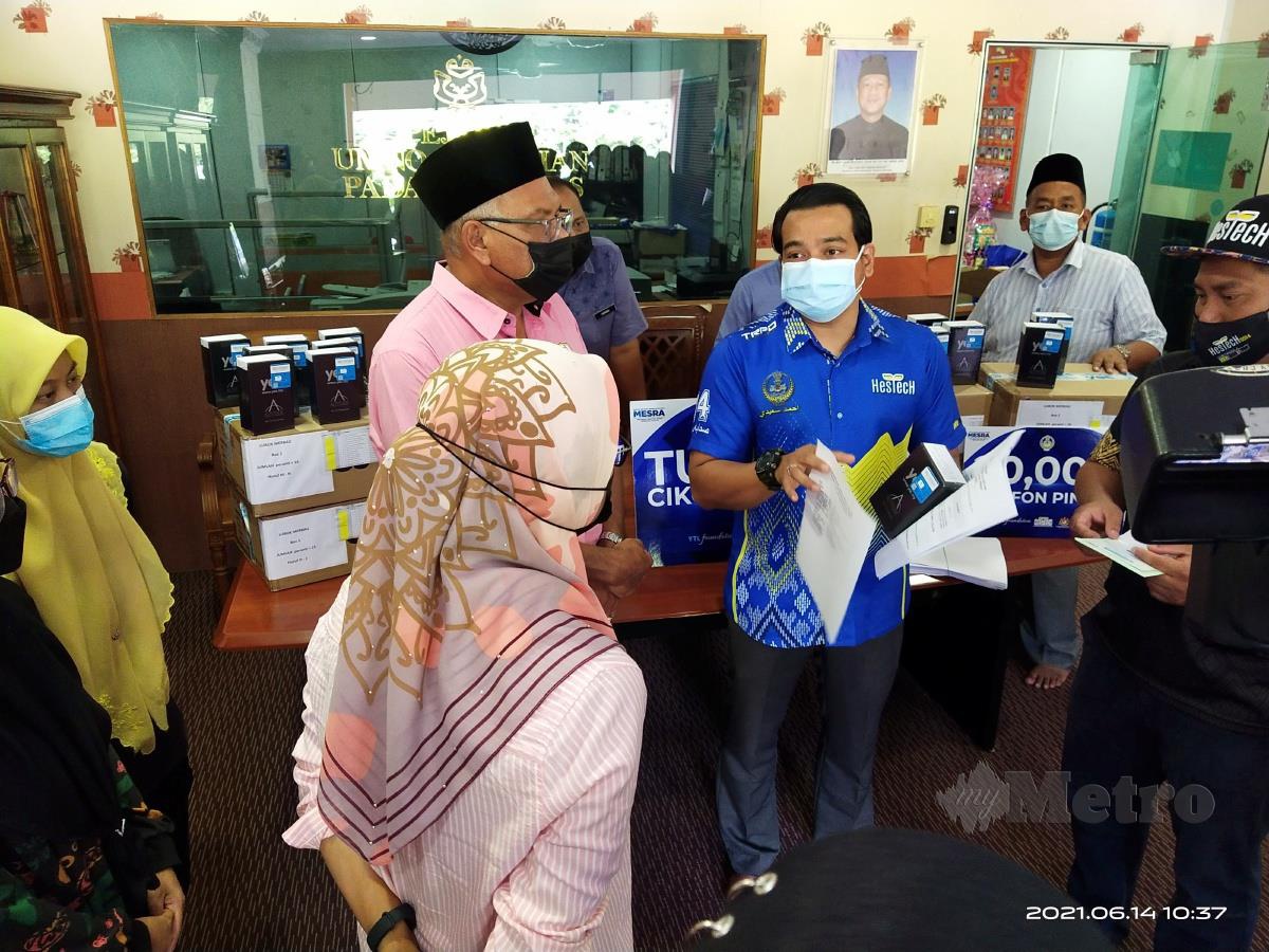 AHMAD Saidi (berbaju biru) mengagihkan bantuan telefon pintar bagi program TCS di Pusat Khidmat DUN Lubuk Merbau, di sini, hari ini. Turut hadir Adun Lubok Merbau, Dr Jurij Jalaludin (kiri). FOTO Muhammad Zulsyamini Sufian Suri