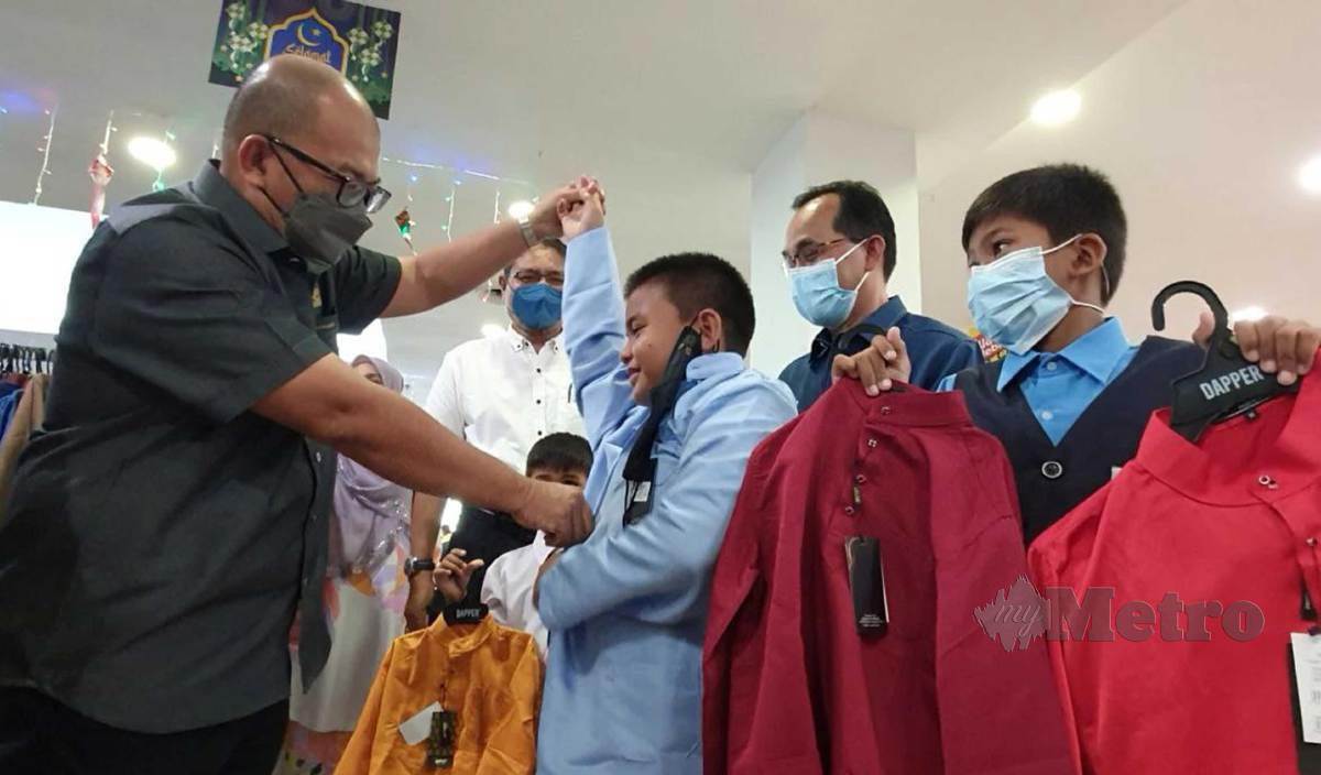 NASARUDDIN (kiri) membantu anak yatim, Muhammad Rizmi Safuan mencuba baju raya pada Program Sinaran Kasih 2022 di Langkawi.  FOTO Hamzah Osman