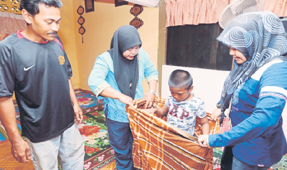 MUNIRAH (dua dari kiri) membetulkan kain pelekat dipakai anaknya, Muhammad Nabil Qayyum Mohd Zaki.