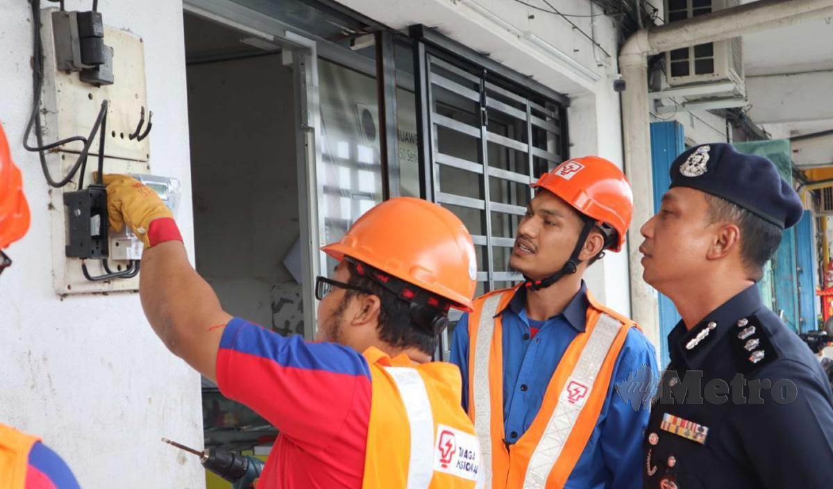 NOR Omar (kanan) melihat petugas TNB melakukan kerja-kerja pemotongan bekalan elektrik di sebuah premis judi di Sitiawan. FOTO Muhamad Lokman Khairi