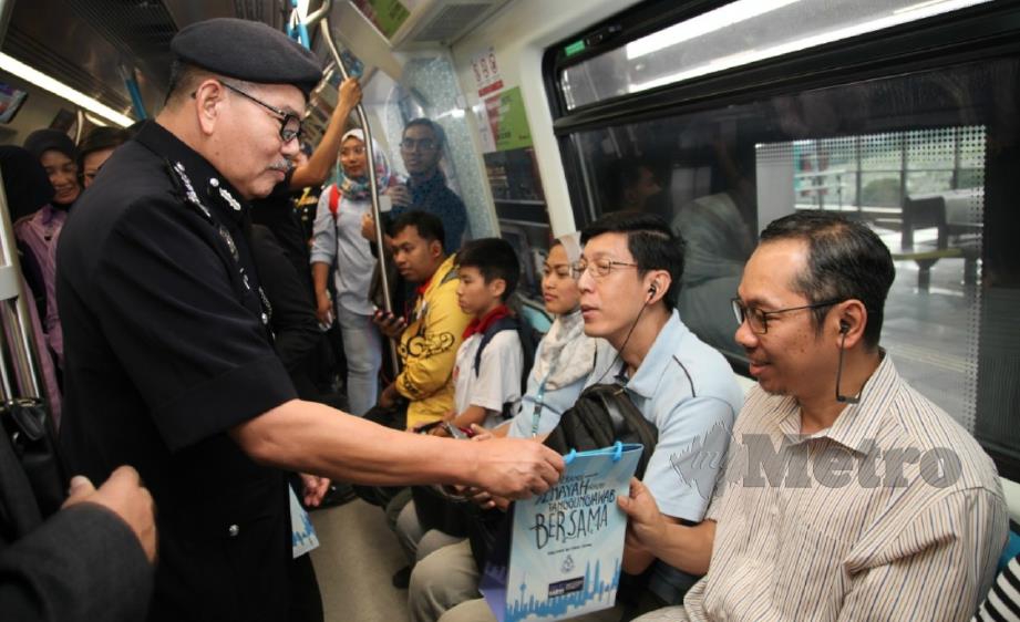 MAZLAN (kiri) mengedarkan risalah mengenai pencegahan jenayah kepada penumpang MRT, hari ini. FOTO ihsan polis.  