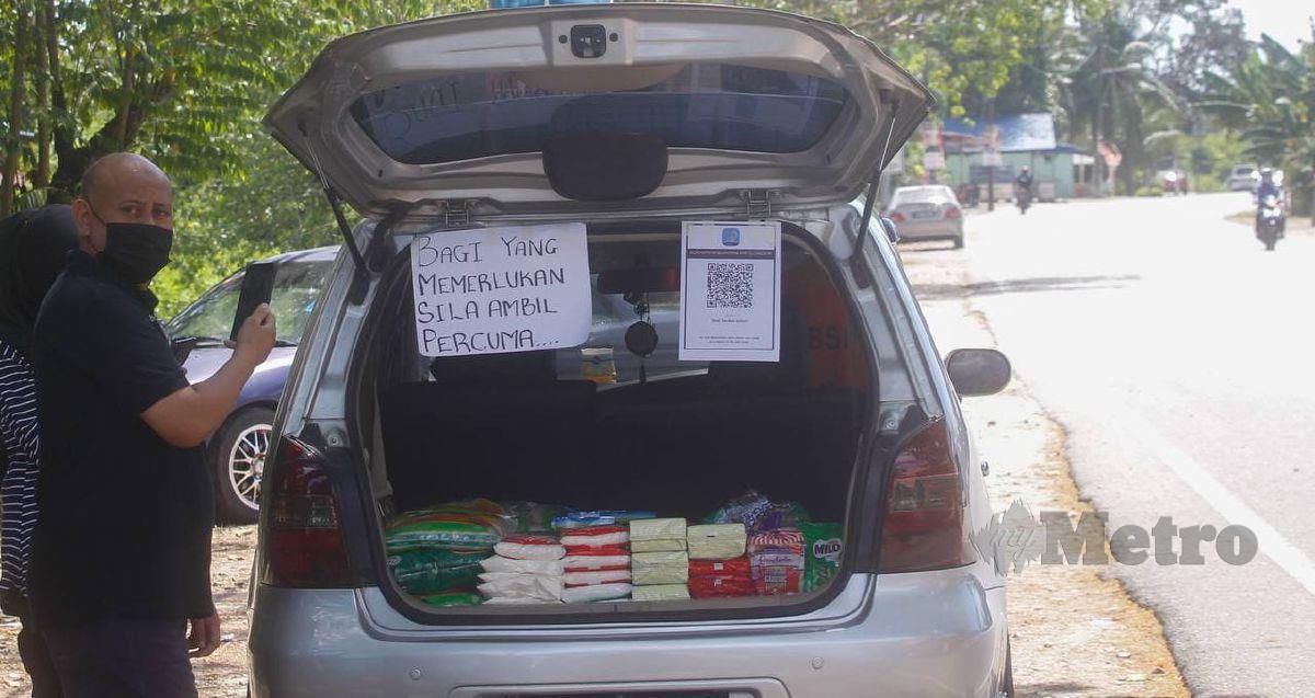 AZIZUL (kiri) membuka but kenderaannya yang diisi dengan pelbagai barangan keperluan secara percuma bagi mereka yang memerlukan. FOTO Danial Saad