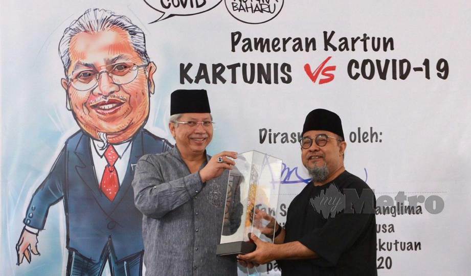 ANNUAR (kiri) menyampaikan Anugerah Komik 2020, Ar Ahmad Hilmy Abdullah selepas merasmikan Pameran Kartun Kartunis vs Covid-19 di Taman Botani Perdana. FOTO Fathil Asri