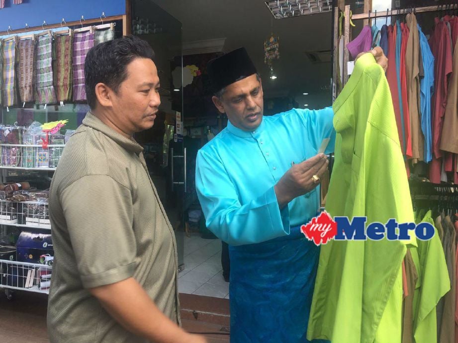 Maideen membelek baju Melayu yang dijual bersama seorang pelanggan di Maroz Keramat AU3. FOTO HM Digital