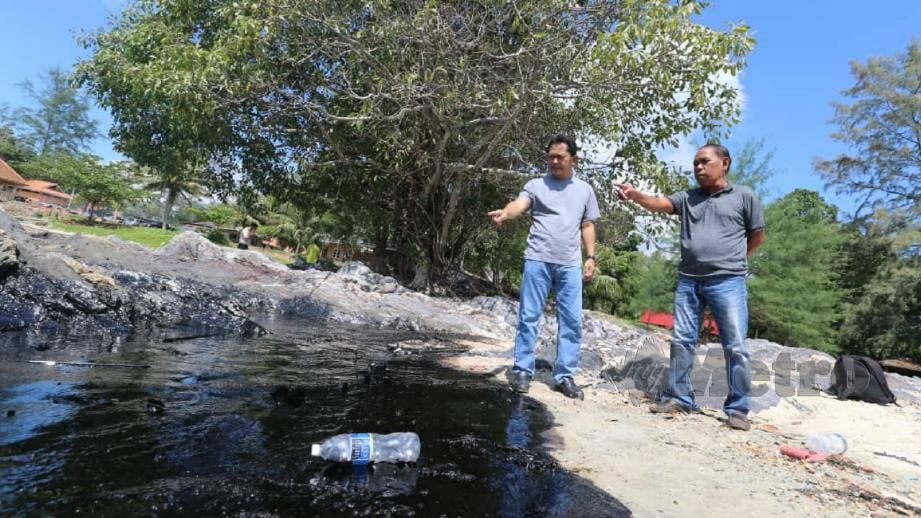 Pengarah Jabatan Laut Johor, Dickson Dollah (kiri) bersama Abu Bakar menunjukkan kesan tumpahan minyak yang sudah merebak ke pesisir Pantai Tanjung Balau. FOTO Zain Ahmed