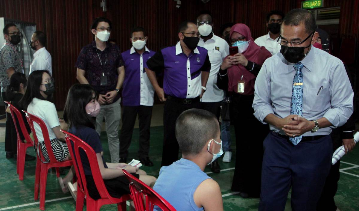 NOOR Azmi (kanan) beramah mesra dengan para pelajar yang menunggu giliran untuk menerima suntikan dos kedua vaksin Covid-19 semasa meninjau proses pemberian vaksin kepada pelajar sekolah di SJK Cina Triang 2. FOTO BERNAMA