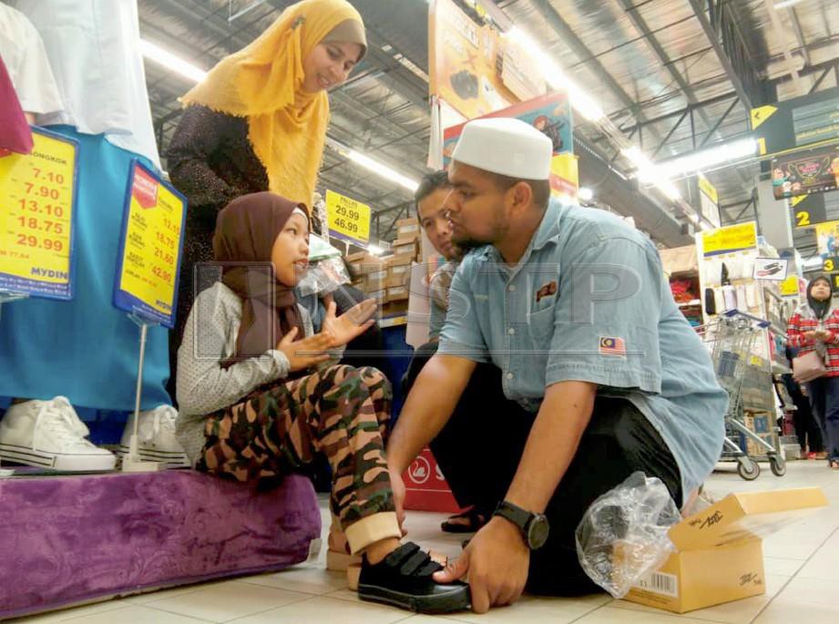 AHMAD Rashdan (kanan) menyarungkan kasut sekolah ke kaki Alia Syarlyn pada Program 'Back To School' (BTS) 2019 anjuran Muslim Care Malaysia. FOTO Nor Farhani Che Ad
