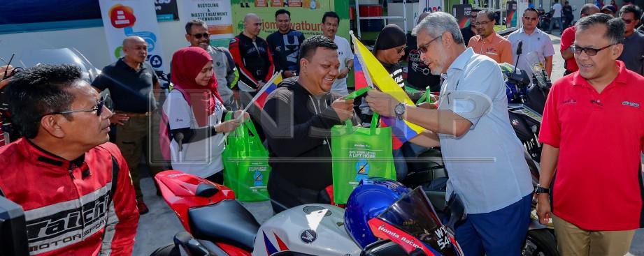 KHALID menyampaikan sebuah beg 'Anti-Litter' kepada penunggang motosikal sambil disaksikan Mohd Zain (kanan). FOTO Aizuddin Saad