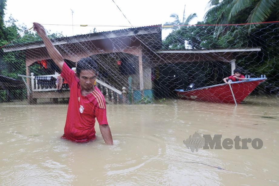 AZWADI memasang pukat di hadapan rumahnya ketika banjir di Kampung Besut. FOTO Ghazali Kori