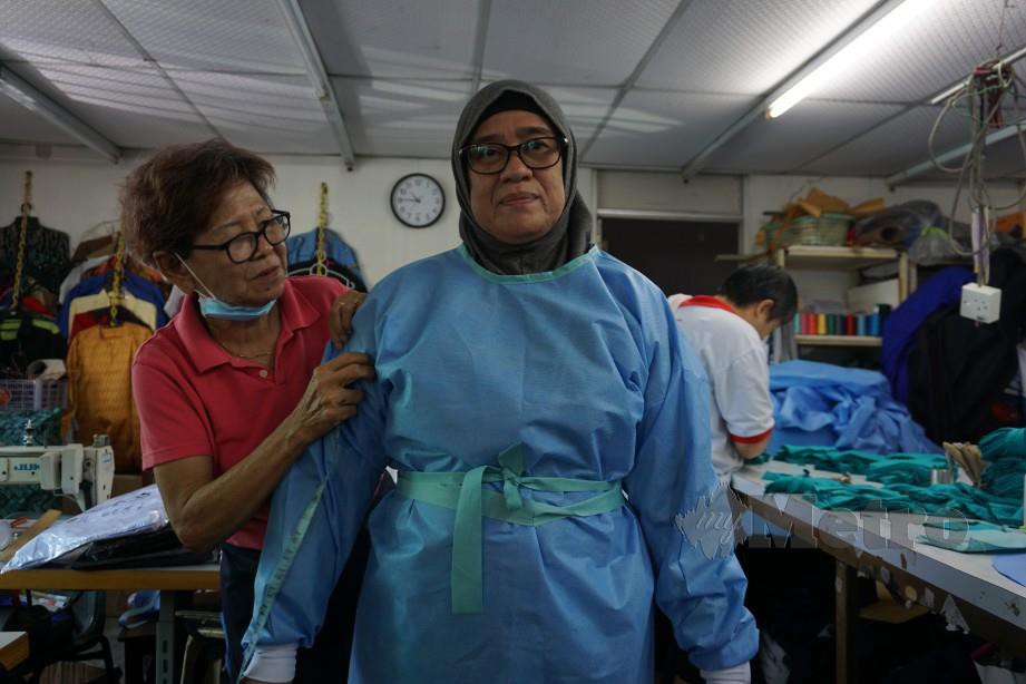 TUKANG jahit, Long Lee Ket (kiri) memeriksa contoh jubah luar PPE buat kegunaan petugas kesihatan. FOTO Bernama