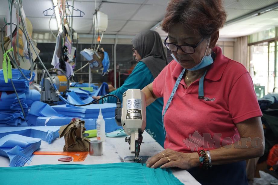TUKANG jahit, Long Lee Ket (kanan) memotong kain untuk dijadikan baju PPE bagi kegunaan petugas kesihatan. FOTO Bernama