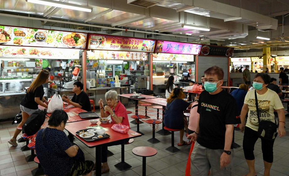 ORANG ramai yang makan di gerai di Singapura mengamalkan penjarakan sosial untuk mengekang penularan Covid-19. FOTO AFP. 
