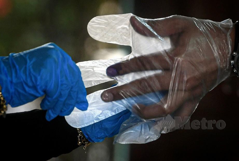 PENGUNDI dipakaikan sarung tangan plastik oleh petugas SPR sebelum mengundi di Kelas Al-Quran dan Fardu Ain (KAFA) Felda Chini 3. FOTO Bernama