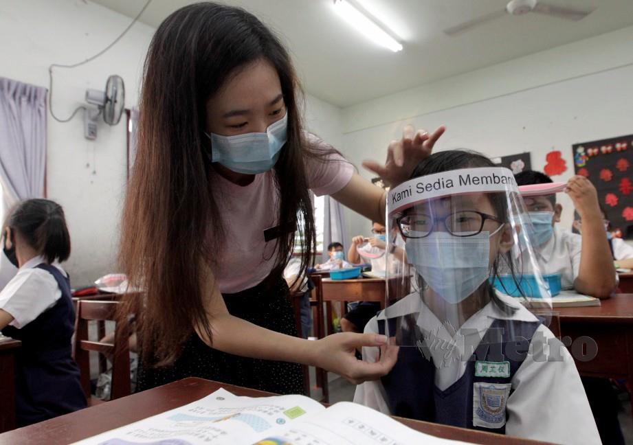 GURU, Ng Zhe Na membantu murid memakai pelindung muka di SJK (C) Jelutong, Georgetown. FOTO Danial Saad