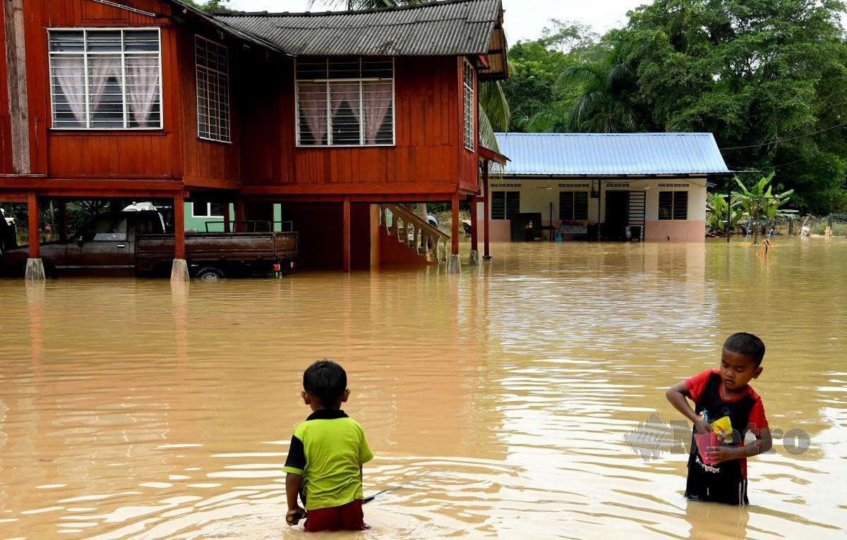 DUA kanak-kanak bermain air banjir di perkarangan  rumah mereka  di Kampung Kuala Sawah, Rantau, semalam. FOTO Bernama