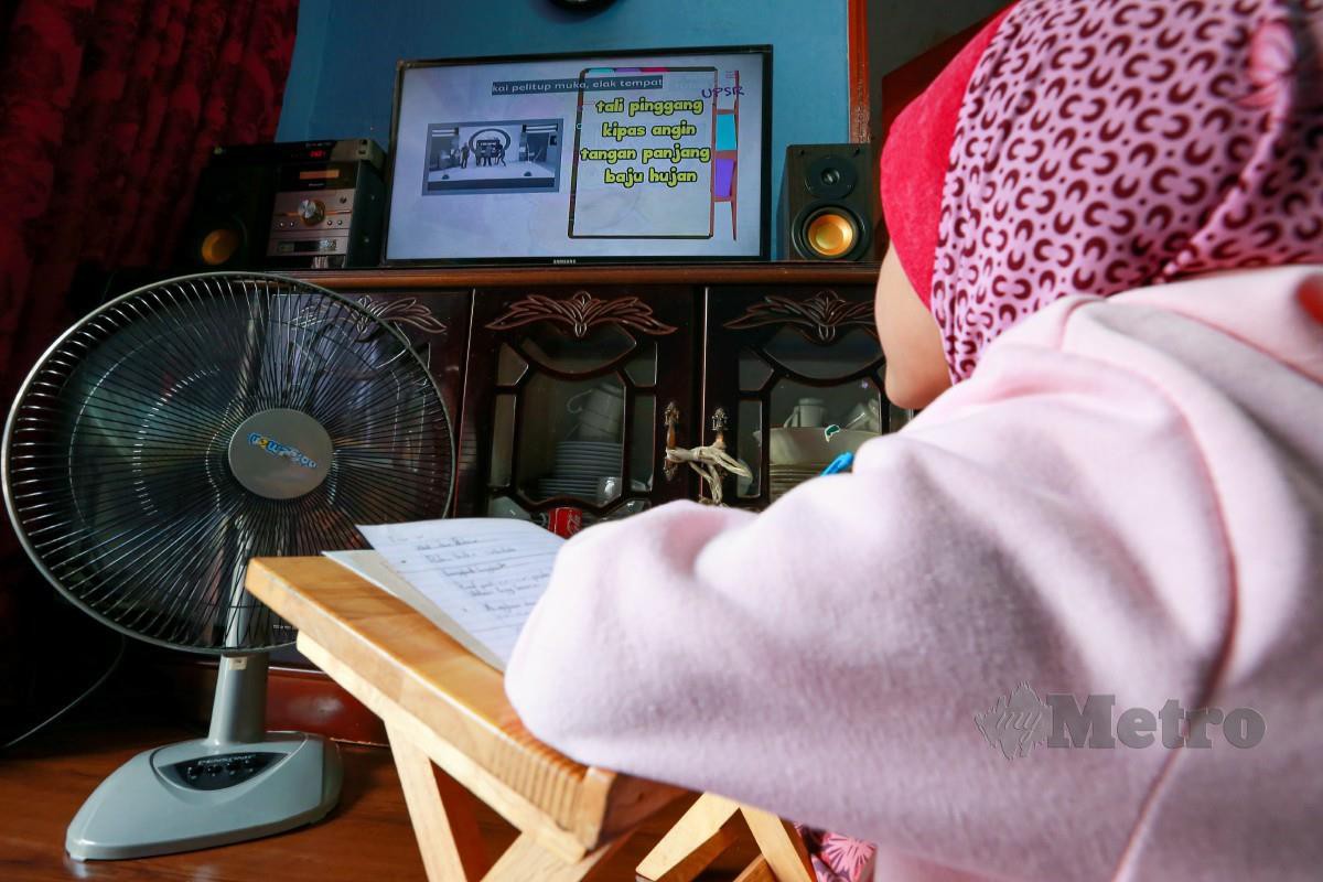 MURID tahun tiga, Aisyah Zarah menonton sambil belajar Bahasa Melayu di rumahnya. FOTO Aswadi Alias