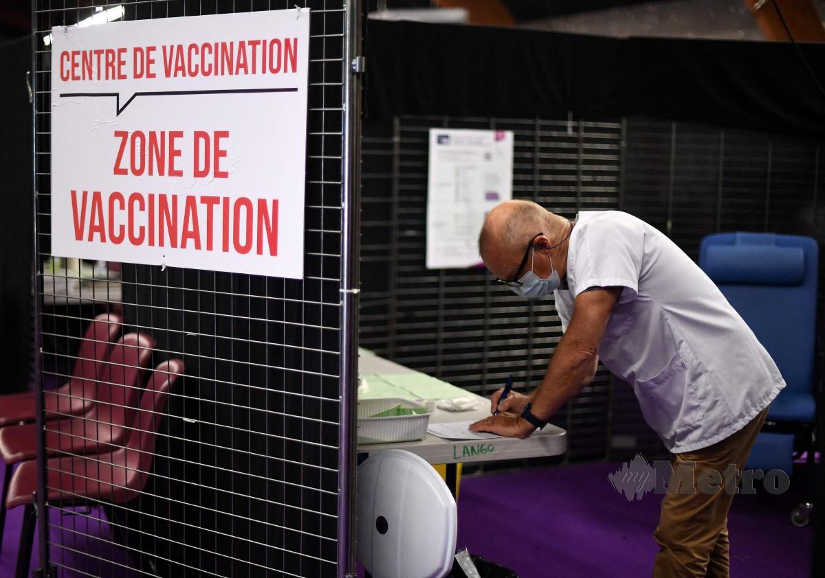 PETUGAS kesihatan menulis nota bersebalah papan tanda yang menyatakan ‘Pusat vaksinasi - zon vaksinasi’ di Perancis pada 31 Mei 2021. Perancis merekodkan peningkatan jumlah pendaftaran janji temu vaksin Covid-19 selepas Macron mengumumkan sekatan ke atas mereka yang tidak divaksin, termasuk ujian mandatori untuk memasuki restoran. FOTO AFP